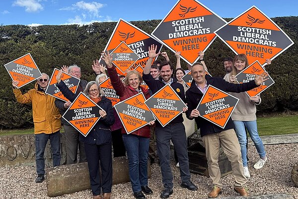 Adam Harley with Susan Murray and Alex Cole-Hamilton in front of Lib Dem campaigners holding orange diamonds