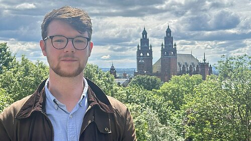 Daniel O'Malley with a green background of trees and the top of Kelvingrove Art Gallery