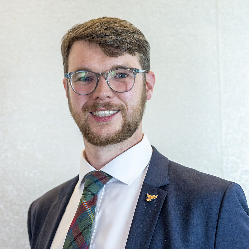 Daniel O'Malley in a suit and tie smiling on a white background.