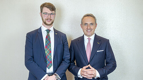 Daniel Khan-O'Malley and Alex Cole-Hamilton standing and smiling in suits.