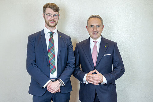 Daniel Khan-O'Malley and Alex Cole-Hamilton standing and smiling in suits.