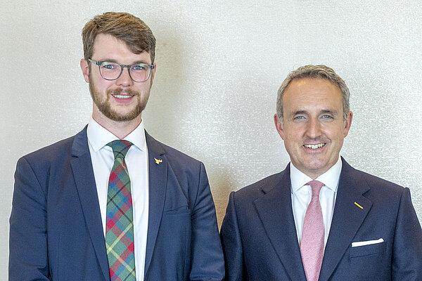 Daniel O'Malley and Alex Cole-Hamilton standing and smiling in suits.