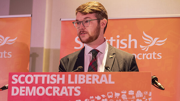 Daniel O'Malley behind a podium which reads Scottish Liberal Democrats on the front